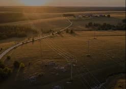 Rede de distribuição de energia atravessando área rural ao pôr do sol